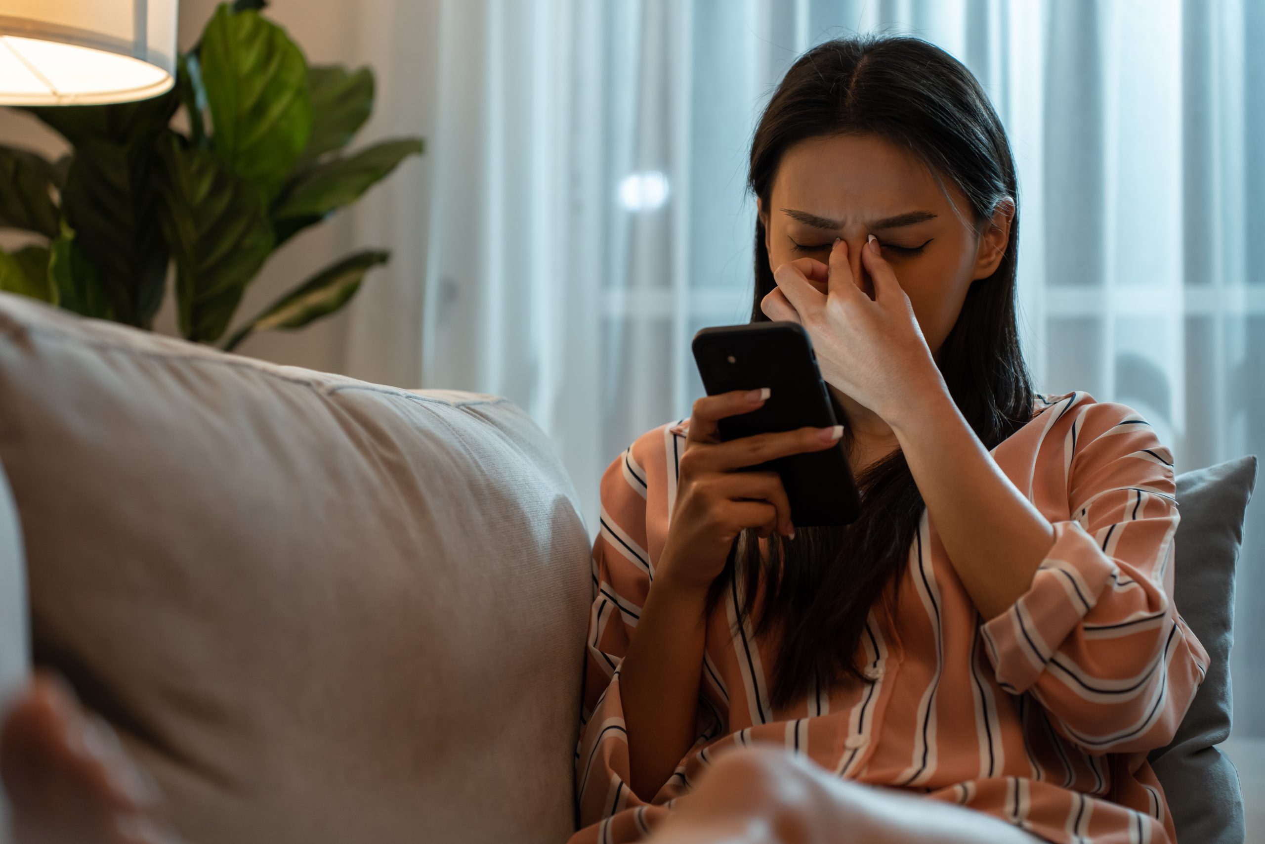 Woman rubbing her eyes while looking at her phone, showing vision discomfort that may indicate retinal problems needing treatment.