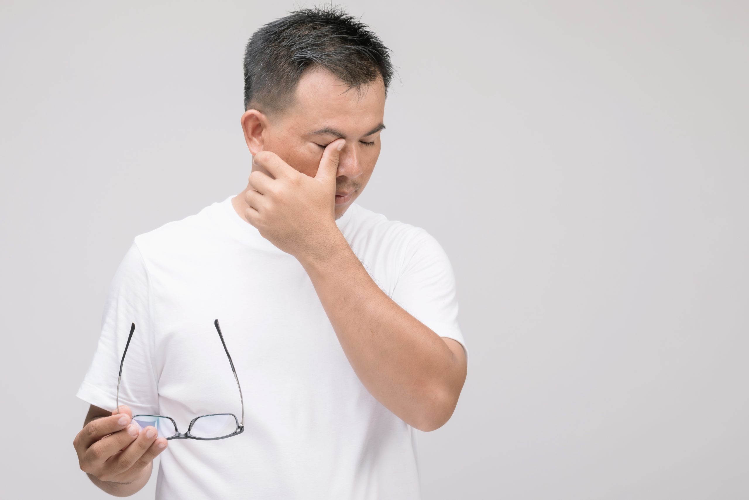 Man rubbing his eye while holding glasses, illustrating possible vision discomfort linked to glaucoma detected through screening in Singapore.